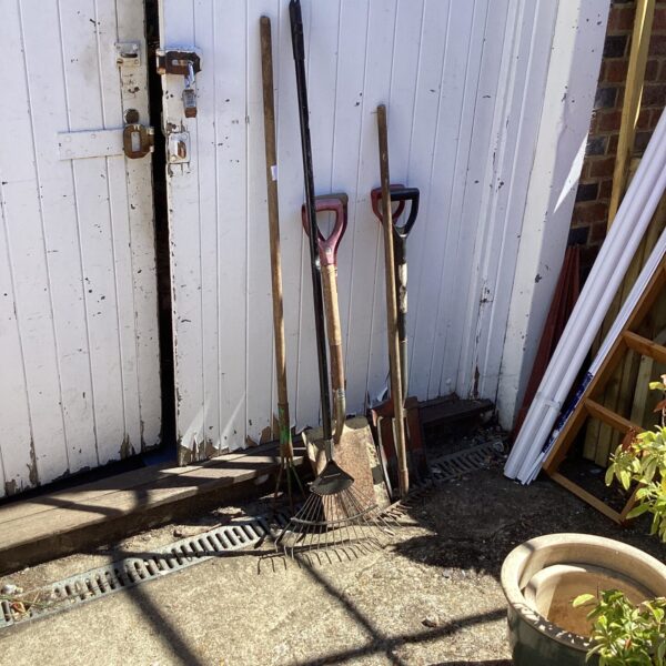 Selection of vintage garden hand tools leaning against a wall.