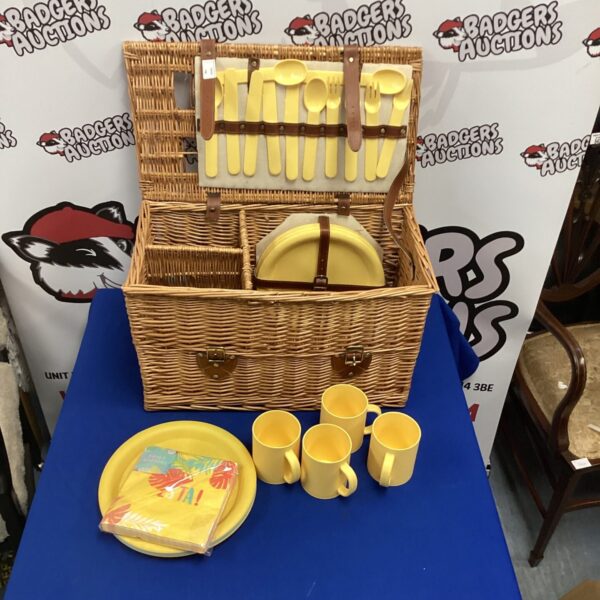 Vintage wicker picnic basket with plates and cups for outdoor dining.
