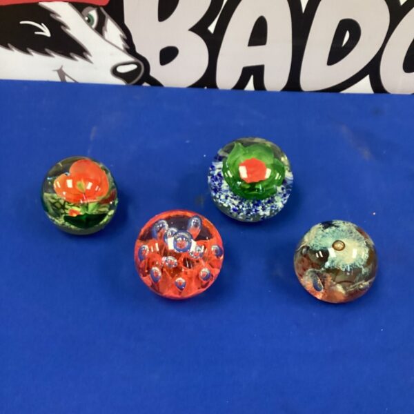 A lot of four colourful Murano glass paperweights on a dark surface.