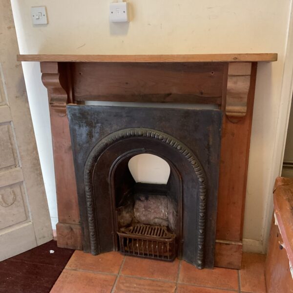 Victorian cast iron fireplace with pine surround in a home setting.