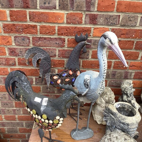 Colourful metal garden cockerels and plastic heron ornament.