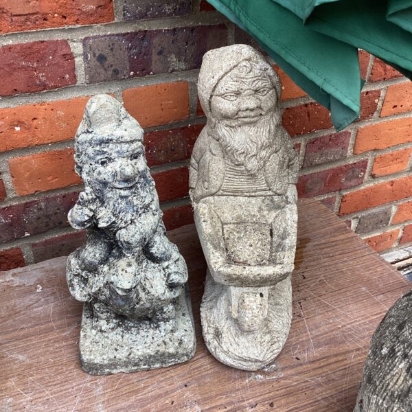 Pair of weathered vintage garden gnome ornaments in a garden.