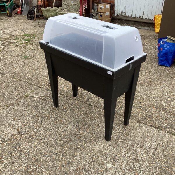 Black plastic greenhouse planter trough in a garden setting.