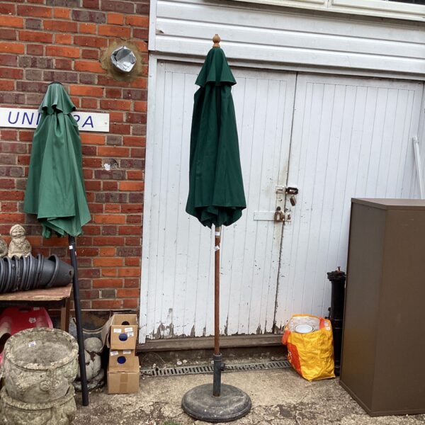 Green patio parasol with black stand in a garden setting.