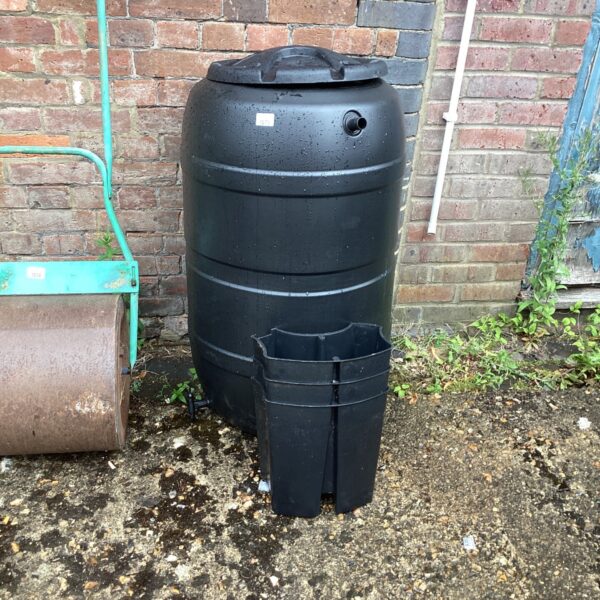 Dark plastic water butt with tap for garden rainwater harvesting.