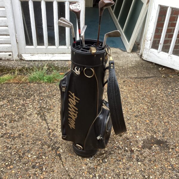 Vintage leather golf bag with antique clubs on a path.