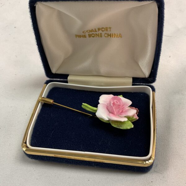Vintage Coalport bone china rose brooch on display case.