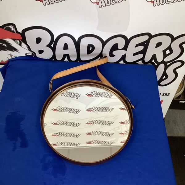 Vintage round wall mirror with leather strap hanging on a wall.