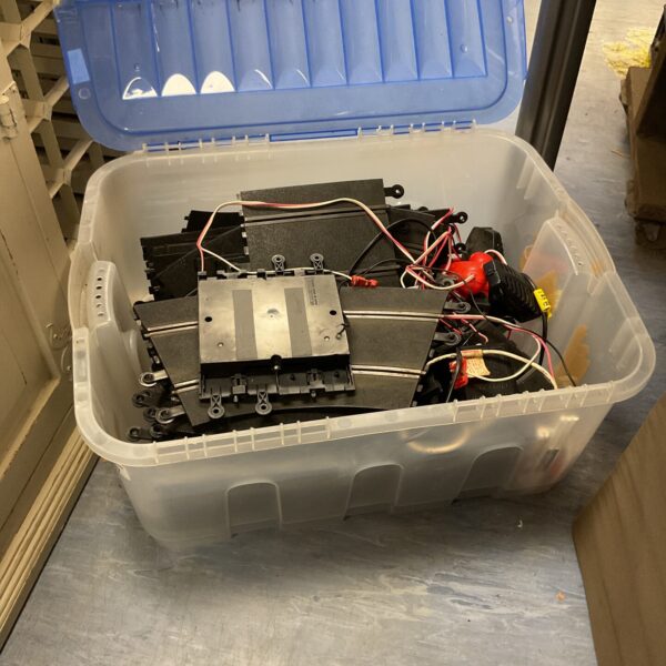 Large plastic storage box filled with Scalextric track pieces and racing accessories.