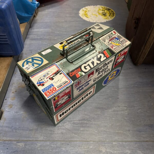 Vintage metal toolbox with motorsport stickers and tools.