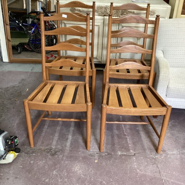 Set of four vintage Ercol Saville dining chairs in warm wood tones.