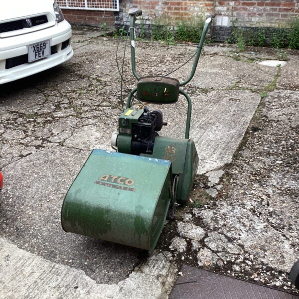 Vintage Atco petrol lawnmower in a garden setting.