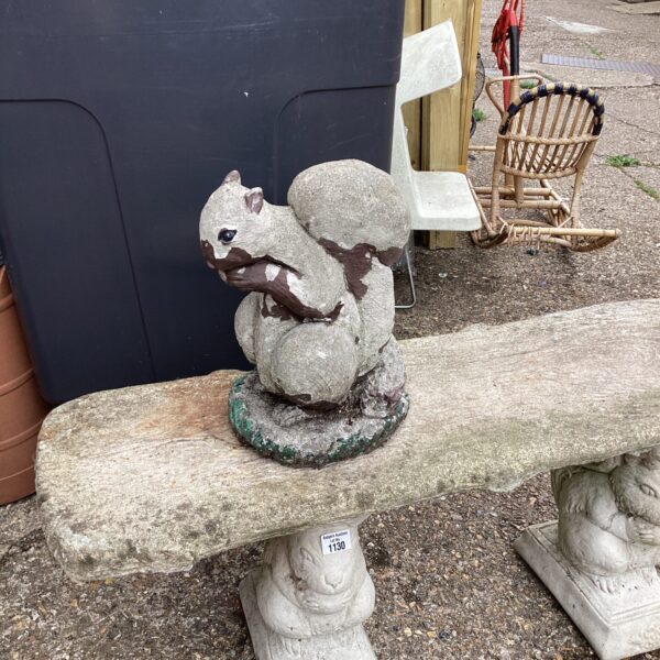 Weathered concrete garden squirrel ornament in a garden setting.
