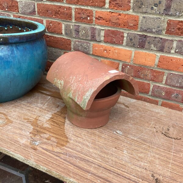 Weathered terracotta chimney cowl in a garden setting.