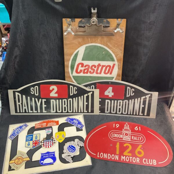 Vintage car rally plates and a wooden timekeepers board with Castrol branding.