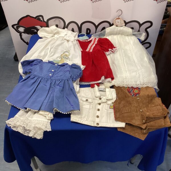 Vintage childrens clothing lot on a blue table, including dresses and waistcoats.