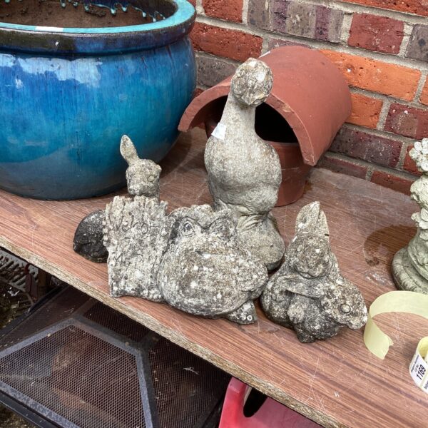 Four small concrete garden ornaments in a garden setting.