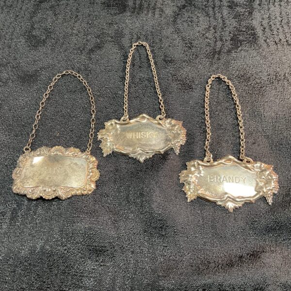Antique silver spirit bottle labels for whiskey, gin, and brandy.