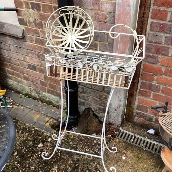 Vintage metal flower trough with hanging basket in garden setting.