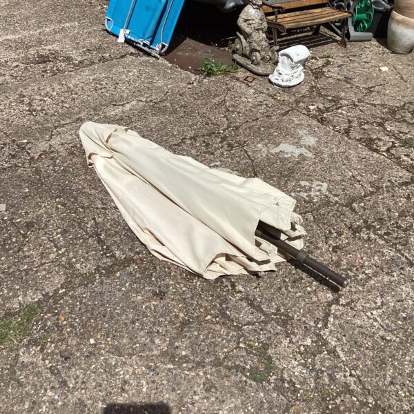 Large patio umbrella in a garden setting, needing repair.