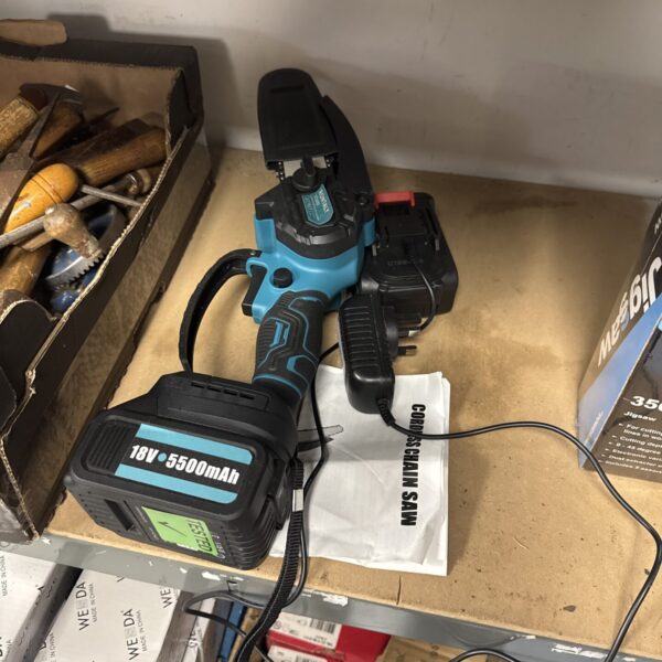 Cordless mini chainsaw with battery and charger for garden tasks.