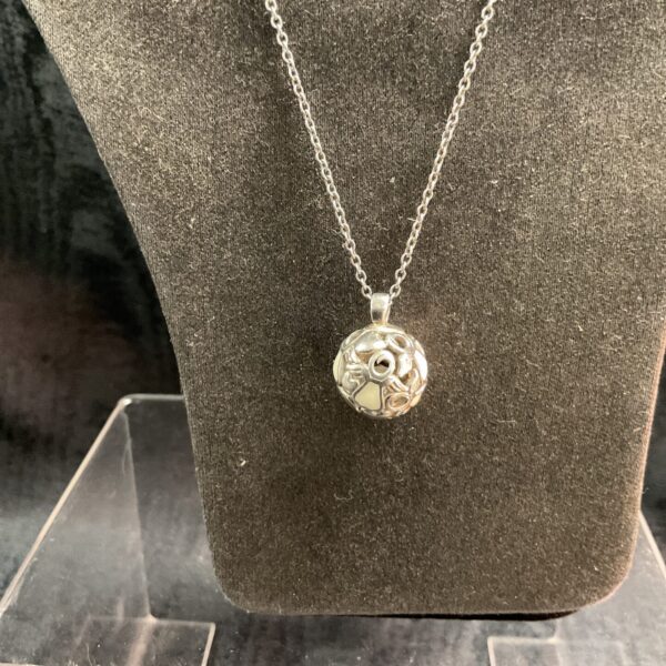 Close-up of silver ball pendant necklace on a dark background.