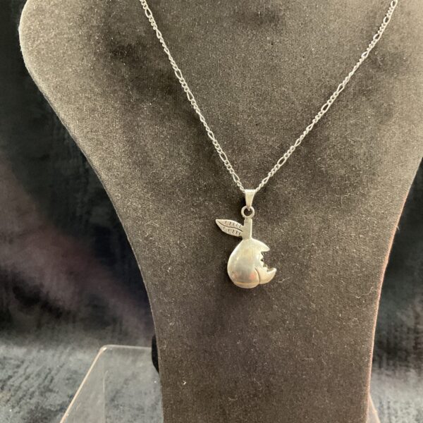 Close-up of a vintage silver apple pendant necklace on a display.
