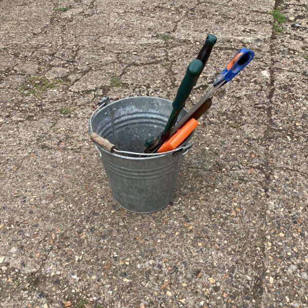Vintage galvanised bucket filled with garden and hand tools.