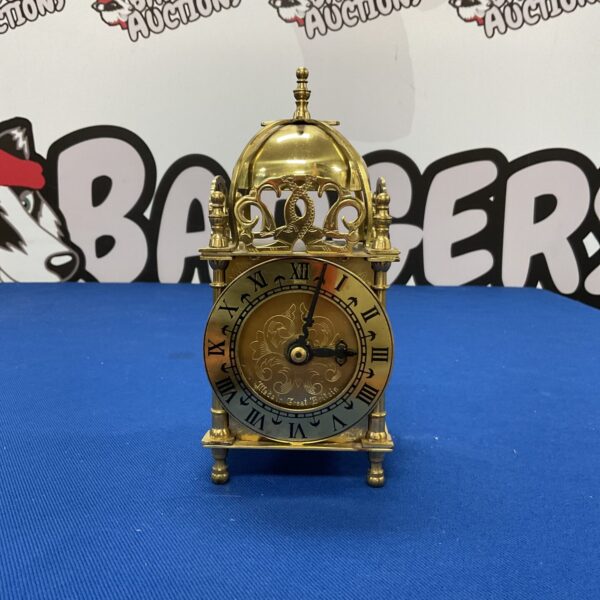 Vintage brass lantern clock with Roman numerals on a white dial.