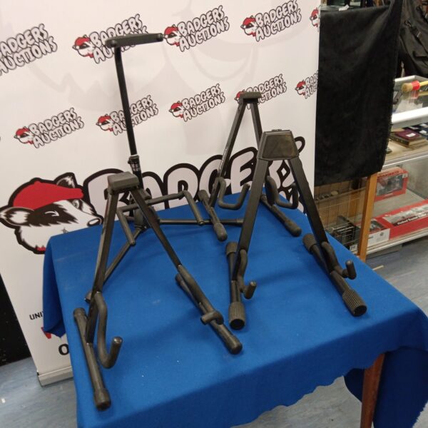 Four black collapsible guitar stands for instrument storage.