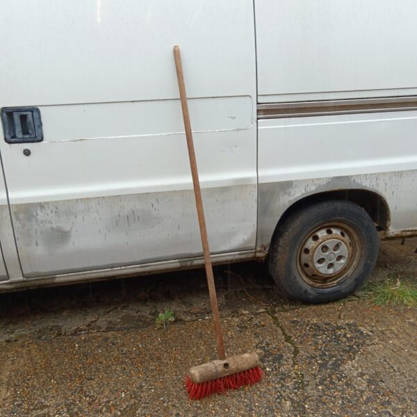 Large yard broom leaning against a vehicle outdoors.