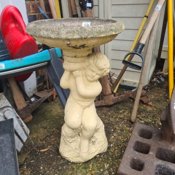 Vintage stone cherub bird bath in a garden setting.