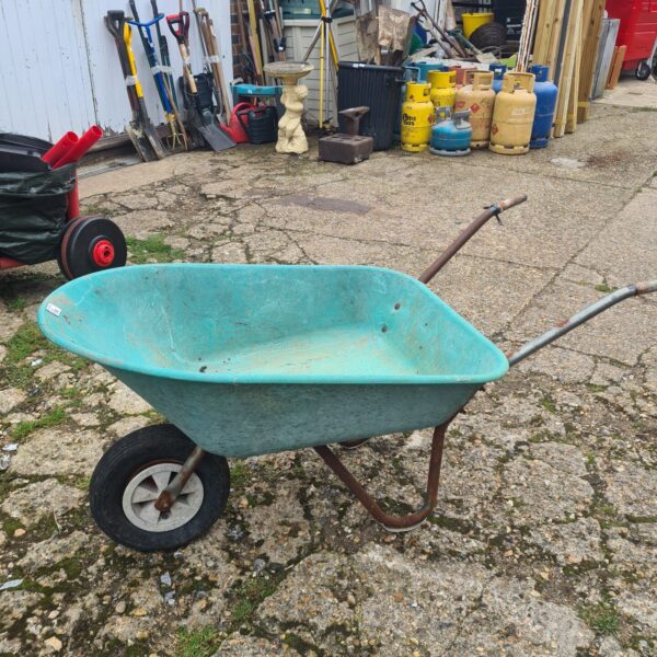 Green plastic wheelbarrow in a garden setting.