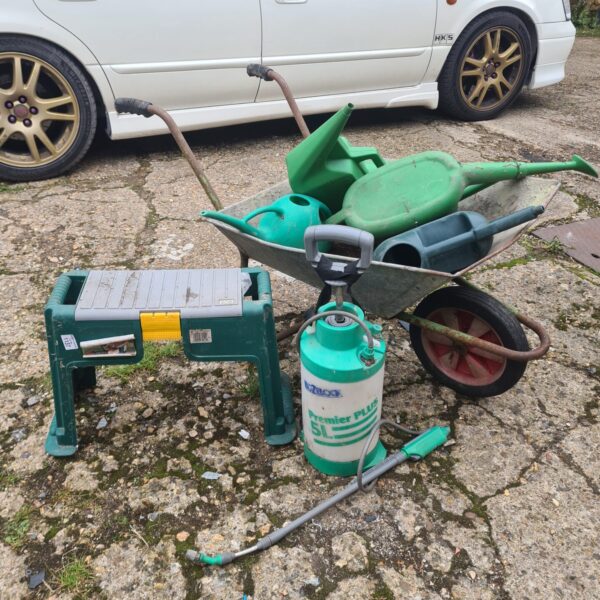 Green garden wheelbarrow with watering can and hose sprayer.