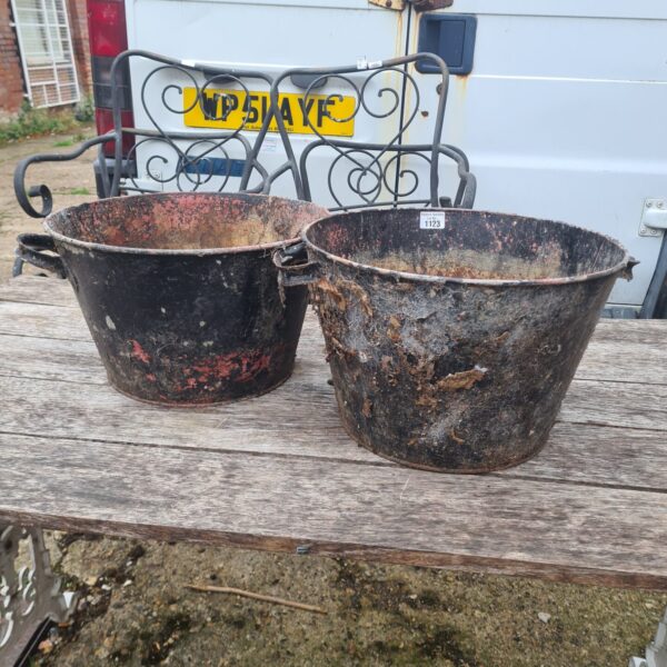 Two weathered vintage cast iron buckets in a garden setting.