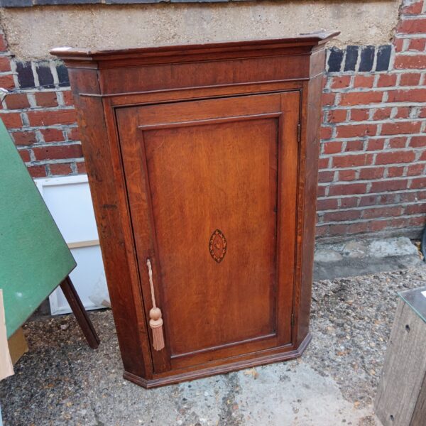 Vintage mahogany corner cabinet with decorative inlay and tassel.