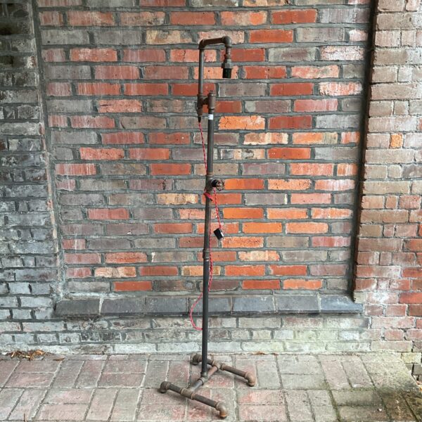 Steampunk floor lamp with metal pipe construction and tripod base.