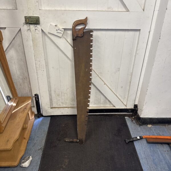 Large vintage logger saw with curved blade and wooden handle.