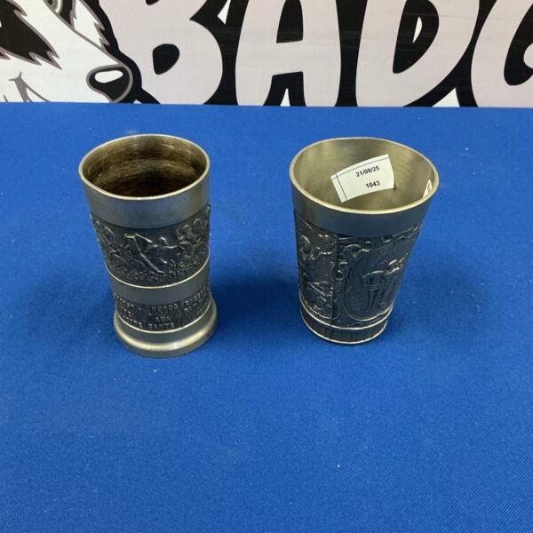Vintage pewter tumblers with embossed detailing, antique barware.