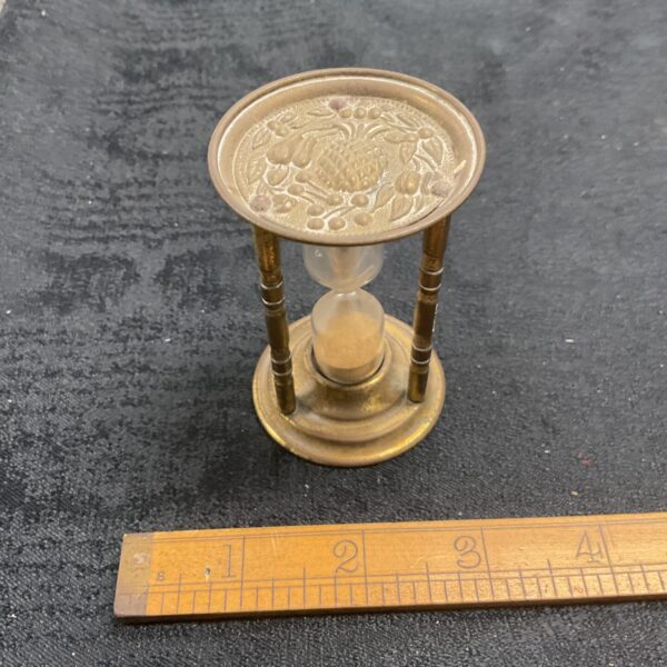Vintage brass hourglass with pineapple decoration on a dark surface.