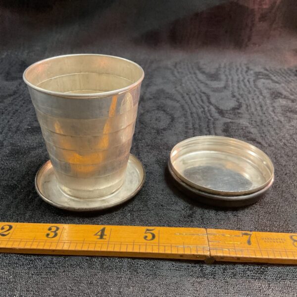 Open vintage whitemetal collapsible cup on ruler.