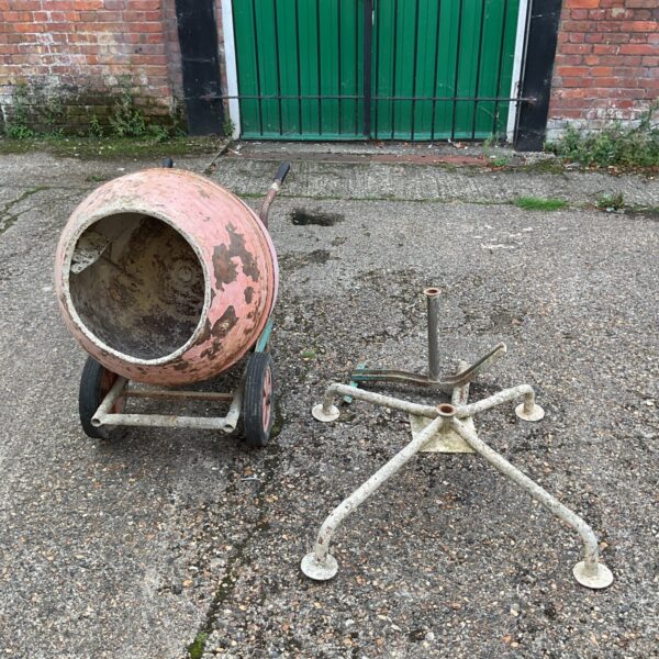 Vintage cement mixer with stand in a garden setting.