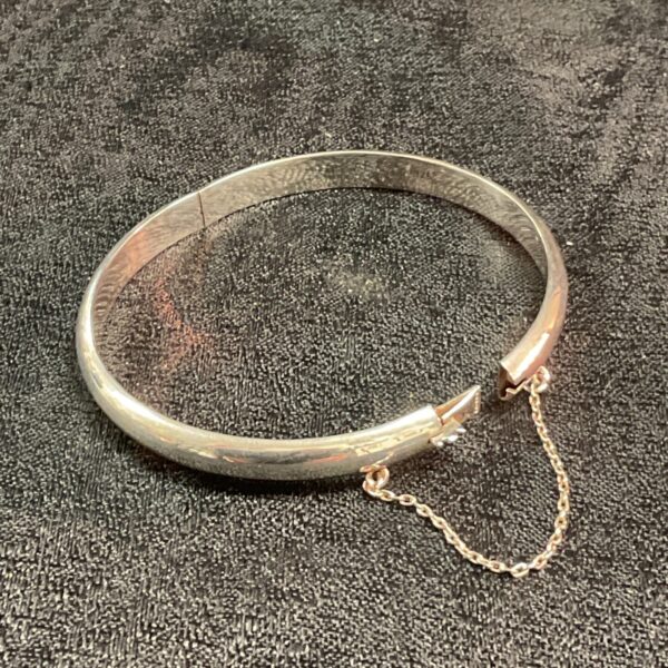 Antique silver hinged bracelet with safety chain detail.