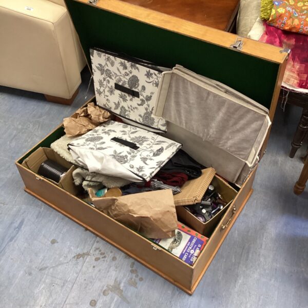 Open wooden storage box filled with fabrics and clothing.