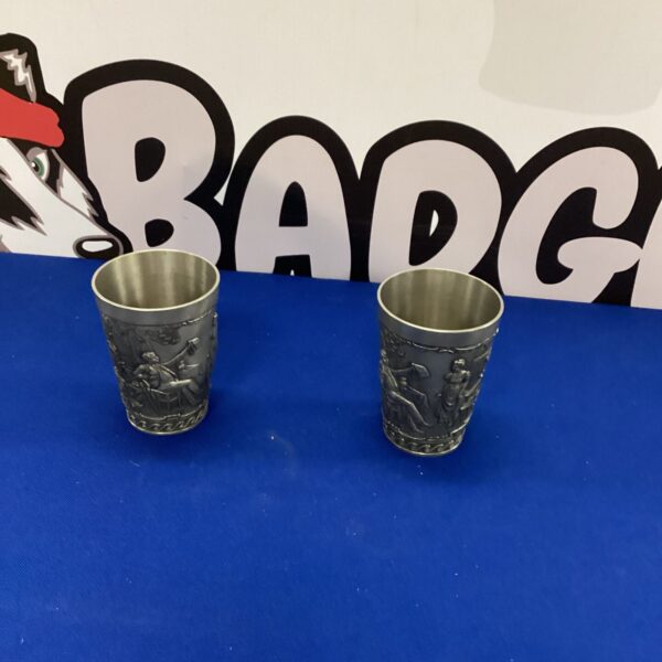 Two vintage pewter tumblers with embossed detailing.