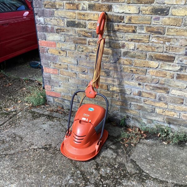 Orange vintage Flymo electric mower in a garden setting.