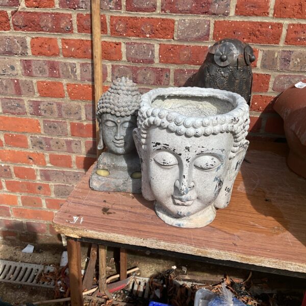 Two weathered stone Buddha head garden ornaments in a garden setting.