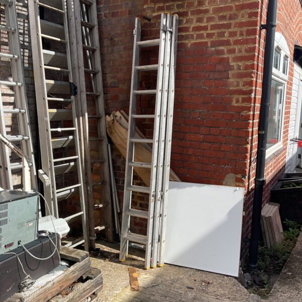 Aluminium three tier extending ladder leaning against brick wall.