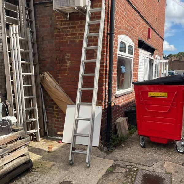 Aluminium extending ladder leaning against a brick wall in a garden.