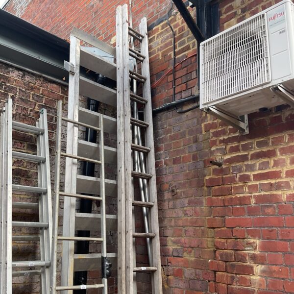 Vintage wooden extension ladder leaning against brick wall.